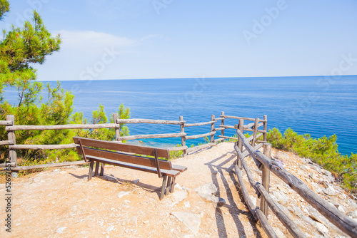 Amazing view of sea nature environment from viewpoint with empty wooden bench. Turquoise color of water. Clear blue sky. Summer landscape.