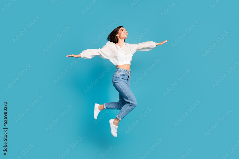 Full length profile portrait of lovely gorgeous person closed eyes arms wings jump fly isolated on blue color background Full length profile portrait of lovely gorgeous person closed eyes arms wings jump fly isolated on blue color background
