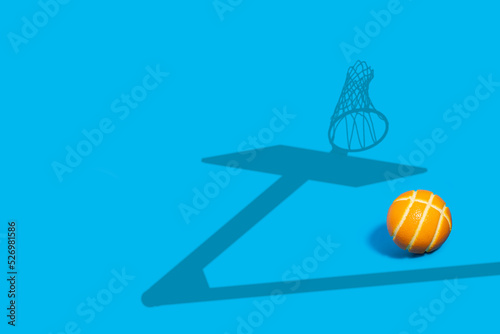 Orange as a basketball on a blue background with a basketball hoop shadow.