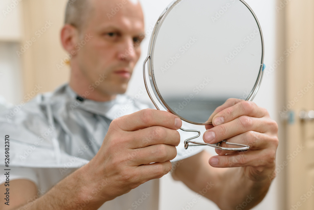 Satisfied man holding mirror and looking on results of his self haircut Satisfied man holding mirror and looking on results of his self haircut