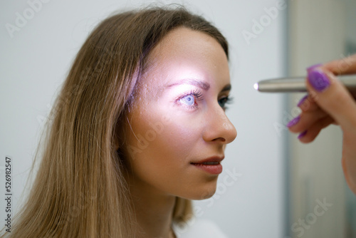 Close up view of doctor testing reflexes of the eye of young woman using a flashlight in medical clinic. Neurological physical examination