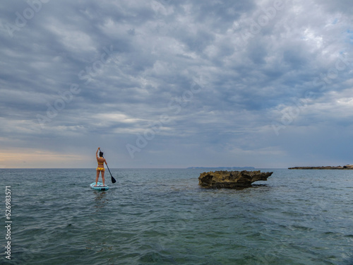 woman paddling on a surfboard under a dramatic sky, Estalella, coast of Llucmajor, Majorca, Balearic Islands, Spain