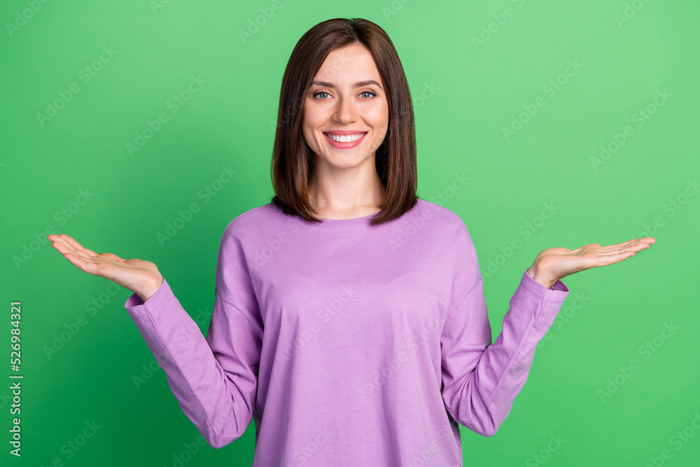 Photo of young happy attractive lady hold two hands compare products low price high quality smiling isolated on green color background Photo of young happy attractive lady hold two hands compare products low price high quality smiling isolated on green color background