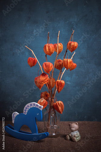 Still life with a bouquet of physalis and a blue wooden horse on a blue background.
