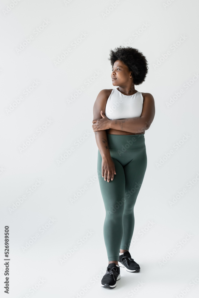 full length of pensive curly african american plus size woman in sportswear standing on white. full length of pensive curly african american plus size woman in sportswear standing on white.