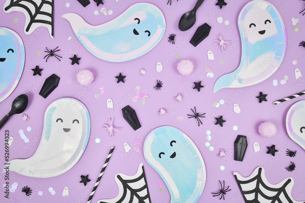 Cute pastel colored Halloween party flat lay with ghost shaped plates, spider web napkins and confetti on violet background Cute pastel colored Halloween party flat lay with ghost shaped plates, spider web napkins and confetti on violet background