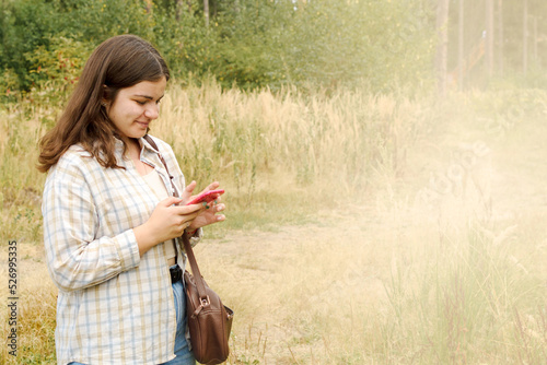 Young happy brown-haired woman in checkered shirt using mobile phone, smiling, space for text.