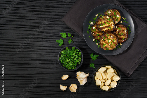 Homemade grilled eggplant with parsley and garlic on a black table, copy space for text.