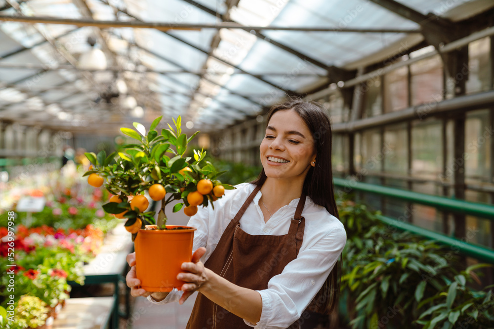 White young woman smiling while holding orange tree in greenhouse White young woman smiling while holding orange tree in greenhouse