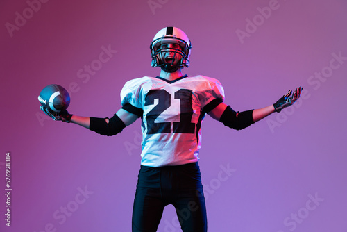 Portrait of emotive man, american football player posing isolated over purple background neon light. Winning championship