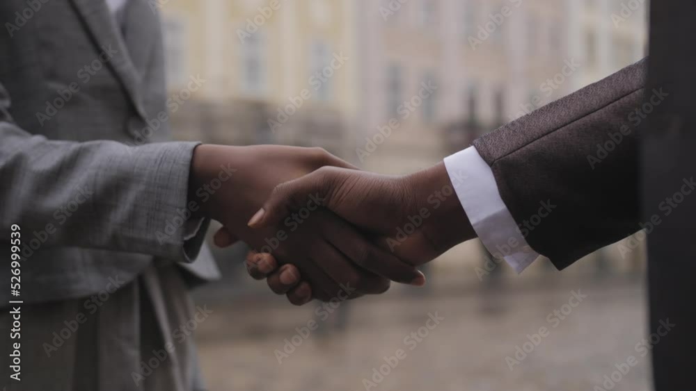 Close up of two afro american partners in formal clothes shaking hands while standing on city street. Man holding leather briefcase, woman holding clipboard.