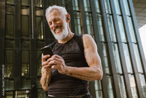 Gray senior man using cellphone while doing workout outdoors