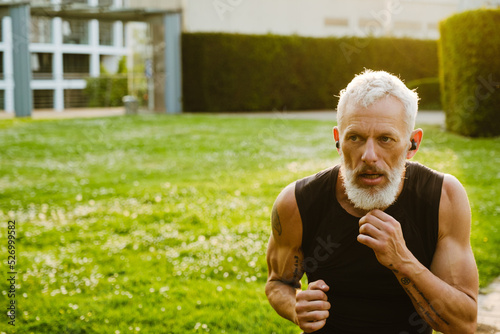Mature gray sportsman wearing earphones boxing in park during workout