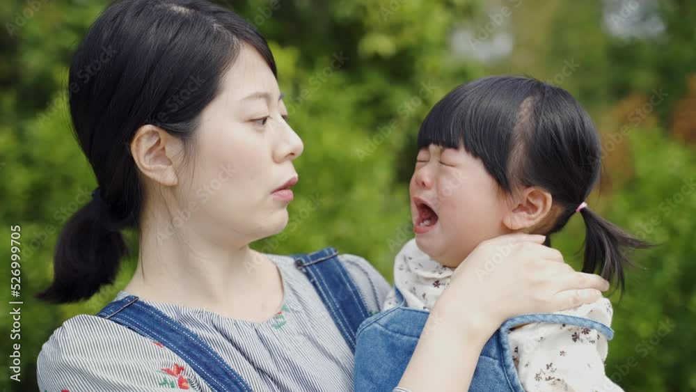 closeup view of a caring Asian mother hugging and patting her upset daughter on the back to console her as she bursts out crying in the park on a sunny day.