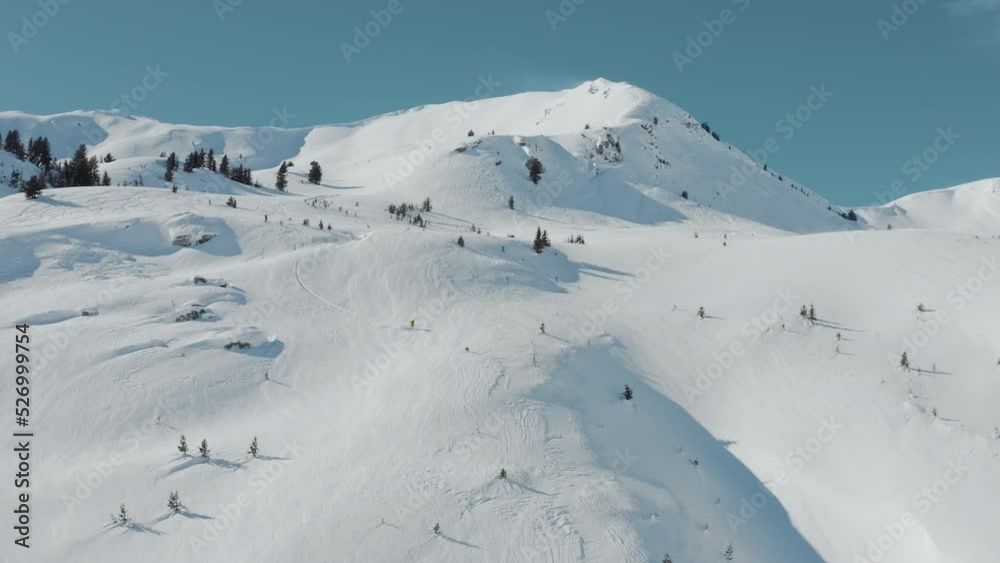 Aerial view of a freestyle snowboarder on a high altitude mountain summit on a sunny winter day. He does spin tricks while riding off-trail fresh powder. Winter Extreme Sports Background Aerial view of a freestyle snowboarder on a high altitude mountain summit on a sunny winter day. He does spin tricks while riding off-trail fresh powder. Winter Extreme Sports Background
