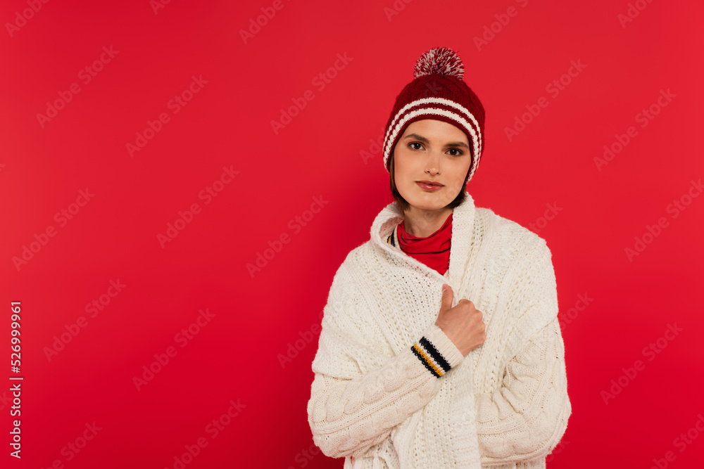 Young woman in knitted clothes looking at camera isolated on red.