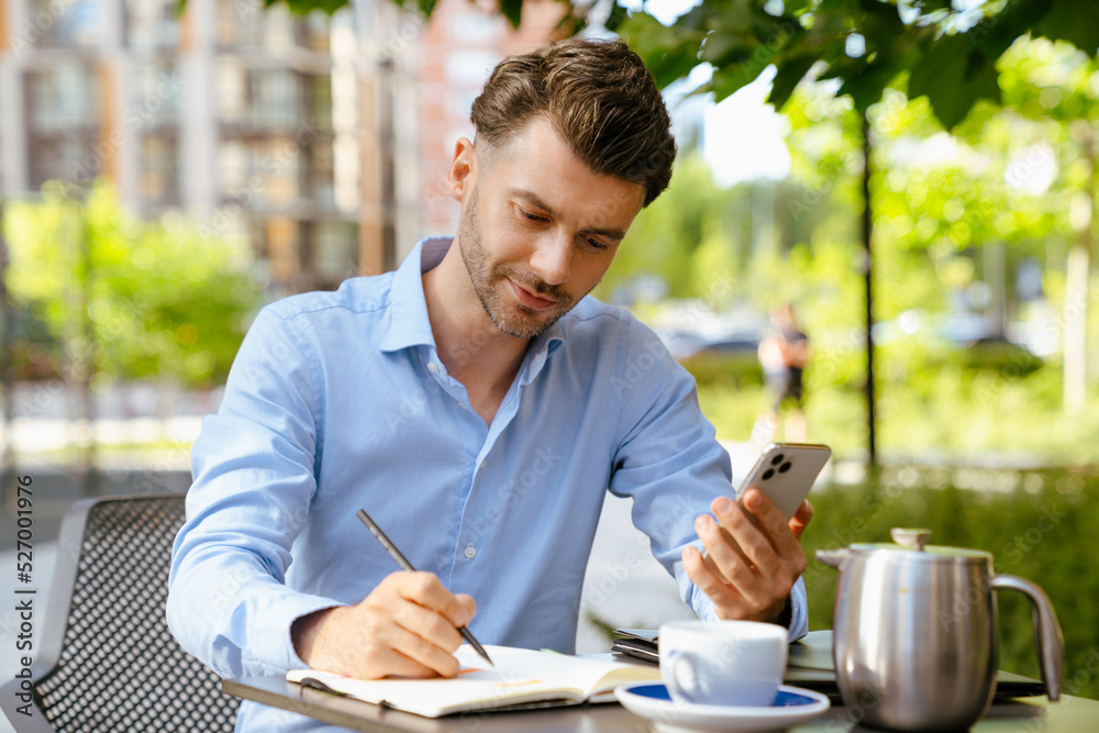 Bristle man using cellphone and writing down notes in cafe outdoors Bristle man using cellphone and writing down notes in cafe outdoors