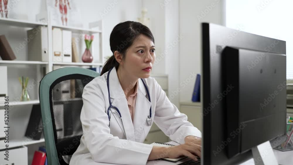 serious asian woman doctor is working and typing on the desktop computer with concentration at desk in the office during daytime. serious asian woman doctor is working and typing on the desktop computer with concentration at desk in the office during daytime.