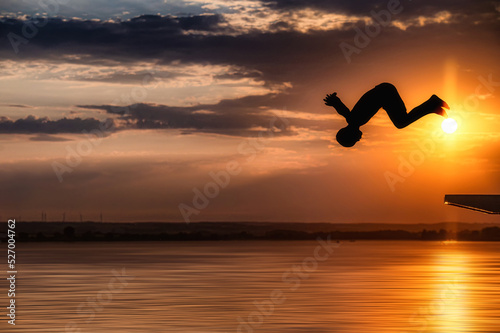 Junge springt an einem wunderschönen Sommerabend mit einem Vorwärtssalto in einen See