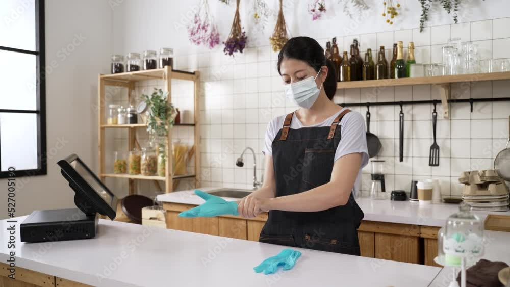 fast forward of an Asian female coffee bar owner in medical mask and apron is putting on protective gloves before working at daytime fast forward of an Asian female coffee bar owner in medical mask and apron is putting on protective gloves before working at daytime