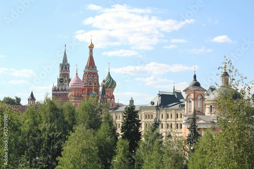 Сolored domes roofs of St. Basil's Cathedral and green trees of Zaryadye Park at summer day at Moscow, Russia. Sun and clouds in the blue sky. 