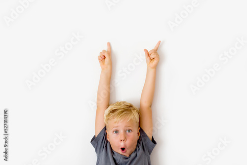 Cute cheerful little blonde boy pointing to empty place on background, preschooler showing copy space for promotional ad.