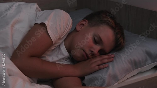 A cute schoolboy sleeps peacefully in a comfortable bed at night in his room.