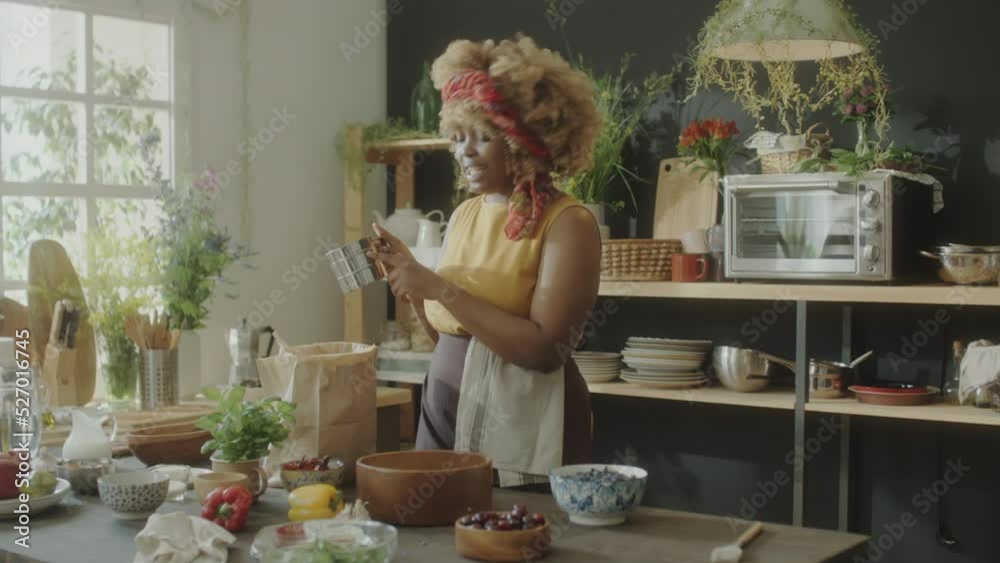 African American female food blogger sifting flour in wooden bowl and talking on camera while filming baking recipe in kitchen African American female food blogger sifting flour in wooden bowl and talking on camera while filming baking recipe in kitchen