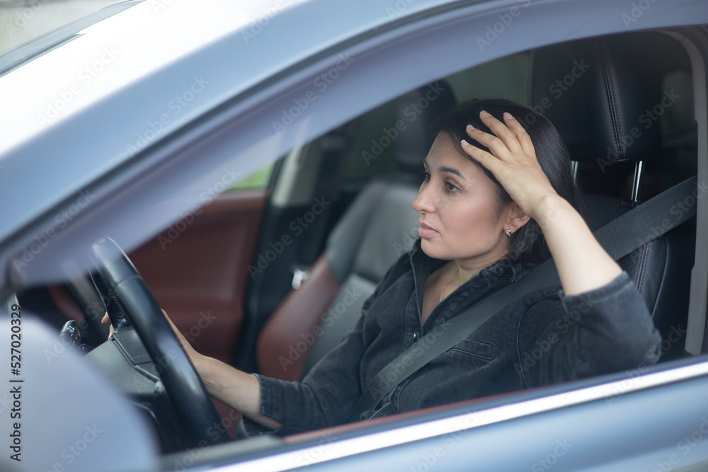 A young tired woman behind the wheel of a car. City traffic jam on the road. Stress, traffic.