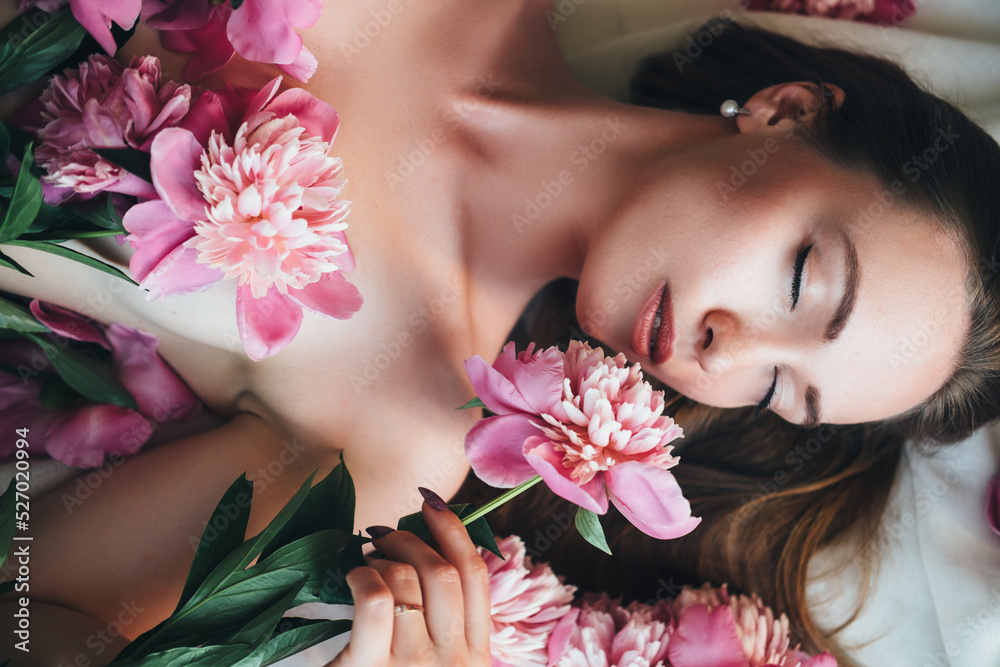 A beautiful woman lies on a white cloth with pink peonies on her body.