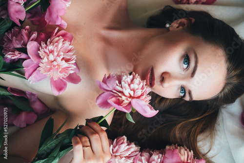 A beautiful woman lies on a white cloth with pink peonies on her body.
