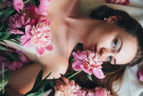 A beautiful woman lies on a white cloth with pink peonies on her body.