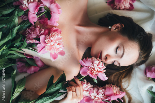 A beautiful woman lies on a white cloth with pink peonies on her body.