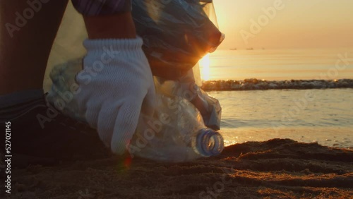 Close-up, a volunteer collects plastic garbage on the beach with gloves and puts it in a garbage bag. Volunteers clean the beach. Cleaning up trash on the beach. 