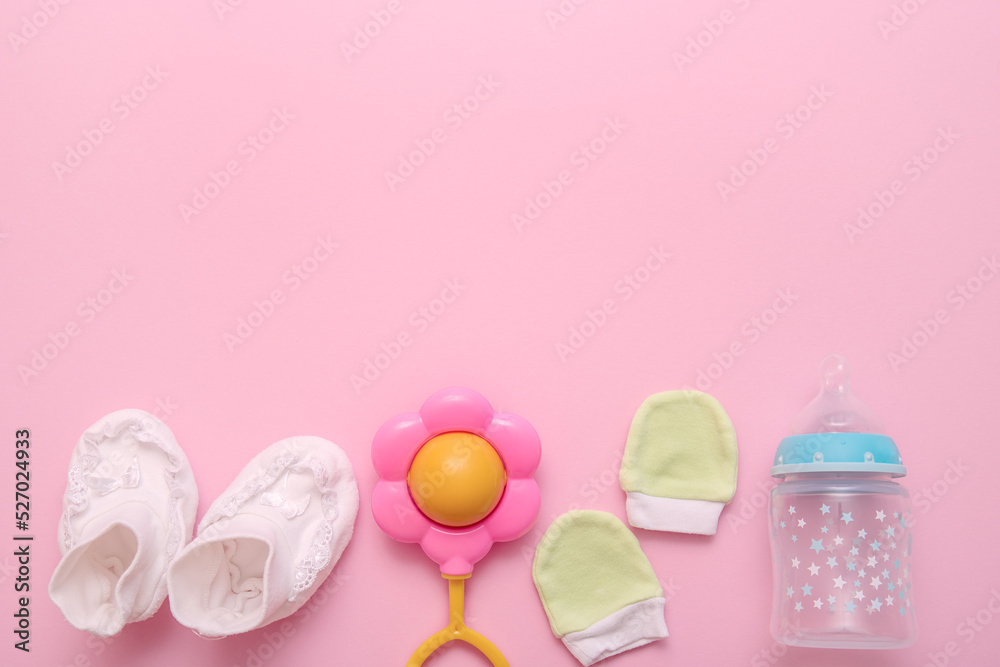 accessories for a newborn - booties, a rattle, a mitten, a bottle for mixture on a pink background with copy space