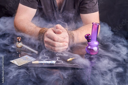 Hostage of cannabis. Drug addiction slavery concept. Bound male hands with smoking devices and weed. photo