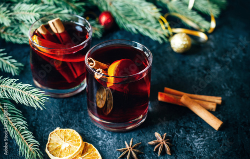 close-up on a hot alcoholic drink mulled wine in two transparent glasses with a cinnamon stick, orange and star anise on a dark  table against the background of Christmas tree branches photo
