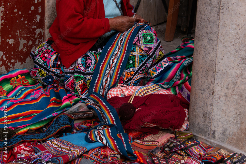 Old woman weaving with her hands, sitting on the ground surrounded by typical Peruvian products, in the town of Pisac, Peru. 