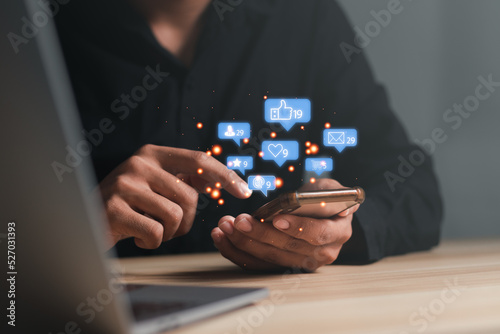 Man using a social media marketing concept on mobile phone with notification icons of like, message, comment and star above smartphone screen.