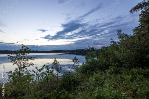 a beautiful blue lake with green tree in the foreground under a dramatic blue dusk sky. High quality photo