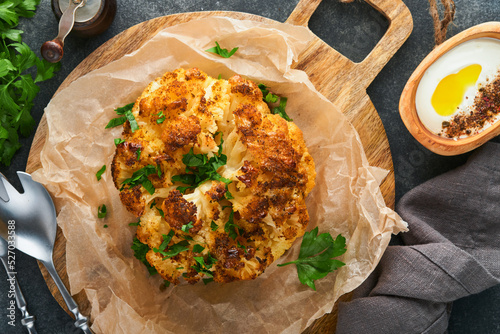 Baked cauliflower. Oven or whole baked cauliflower spices and herbs server on wooden rustic board on old gray background table. Delicious cauliflower. Eyal Shani dish. Perfect tasty snack. photo