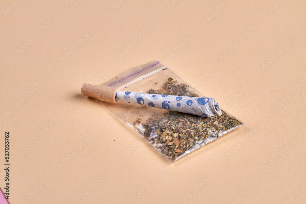 Close-up joint and packet of weed isolated on beige background. Marijuana smoking accessories.