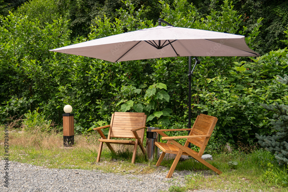 Fashionable outdoor recreation in the forest. Two wooden chairs under an umbrella in the forest. Glamping outdoors.