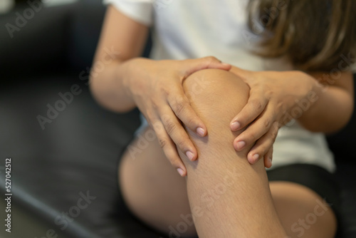 Young woman sitting on sofa and feeling knee pain.