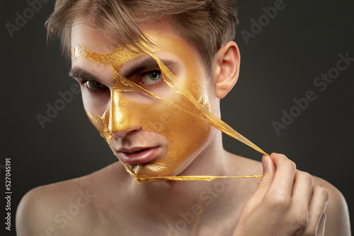 Golden mask on the face of a young handsome guy, for cleansing and rejuvenating the skin. Cosmetological treatment of problem skin of the face and body.