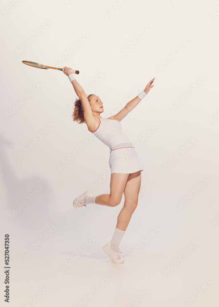 Fototapeta premium Portrait of young spowrtive woman in white uniform playing badminton isolated over grey studio background