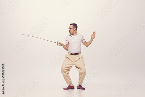 Portrait of man in a suit posing, fighting with swords in a jump isolated over grey studio background © Lustre