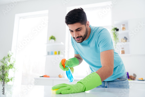 Portrait of neat young guy hold cleaning detergent bottle rag polishing table kitchen indoors