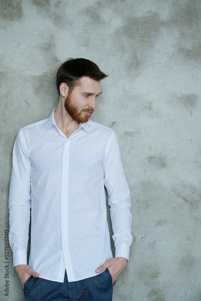 Handsome young man in a white shirt posing on grey wall Handsome young man in a white shirt posing on grey wall