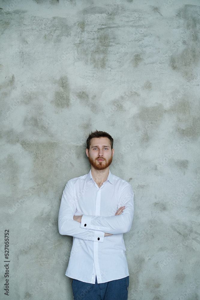 Handsome young man in a white shirt posing on grey wall